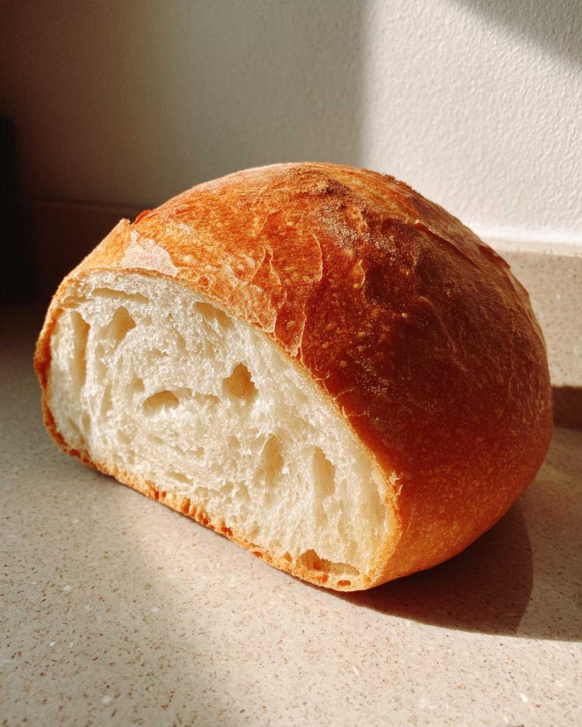 A loaf of crusty bread cut in half, showing the airy interior crumb structure perfect for bread bowls.