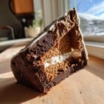 Cross-section view of a sturdy gingerbread house recipe piece showing dark and light gingerbread layers with white icing filling.