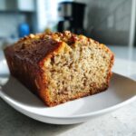 A freshly baked loaf of sugar free banana bread, sliced to show the moist texture and topped with chopped walnuts.