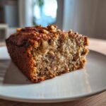 Close-up of a moist slice of sugar free banana bread topped with walnuts, resting on a white plate.