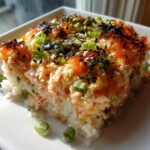 A square serving of baked salmon sushi bake topped with furikake, sesame seeds, and green onions.