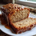 A loaf of sweet alabama pecan bread, partially sliced, covered in a thick, dripping caramel pecan glaze.