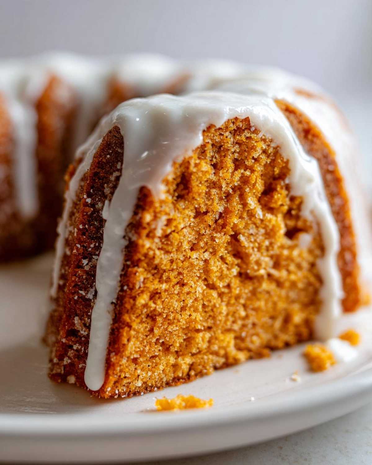 Close-up of a moist slice of orange sweet potato pound cake topped with thick white glaze.