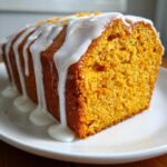 Close-up of a slice of moist sweet potato pound cake topped with thick white vanilla glaze and orange zest.