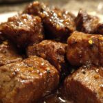 Close-up of tender crockpot steak bites coated in a glossy, savory brown sauce with visible spices.