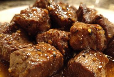 Close-up of tender crockpot steak bites coated in a glossy, savory brown sauce with visible spices.