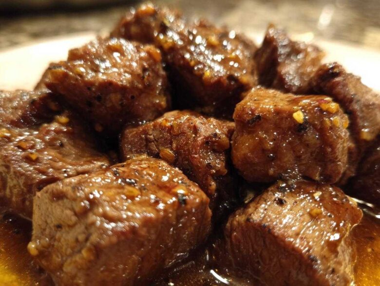 Close-up of tender crockpot steak bites coated in a glossy, savory brown sauce with visible spices.