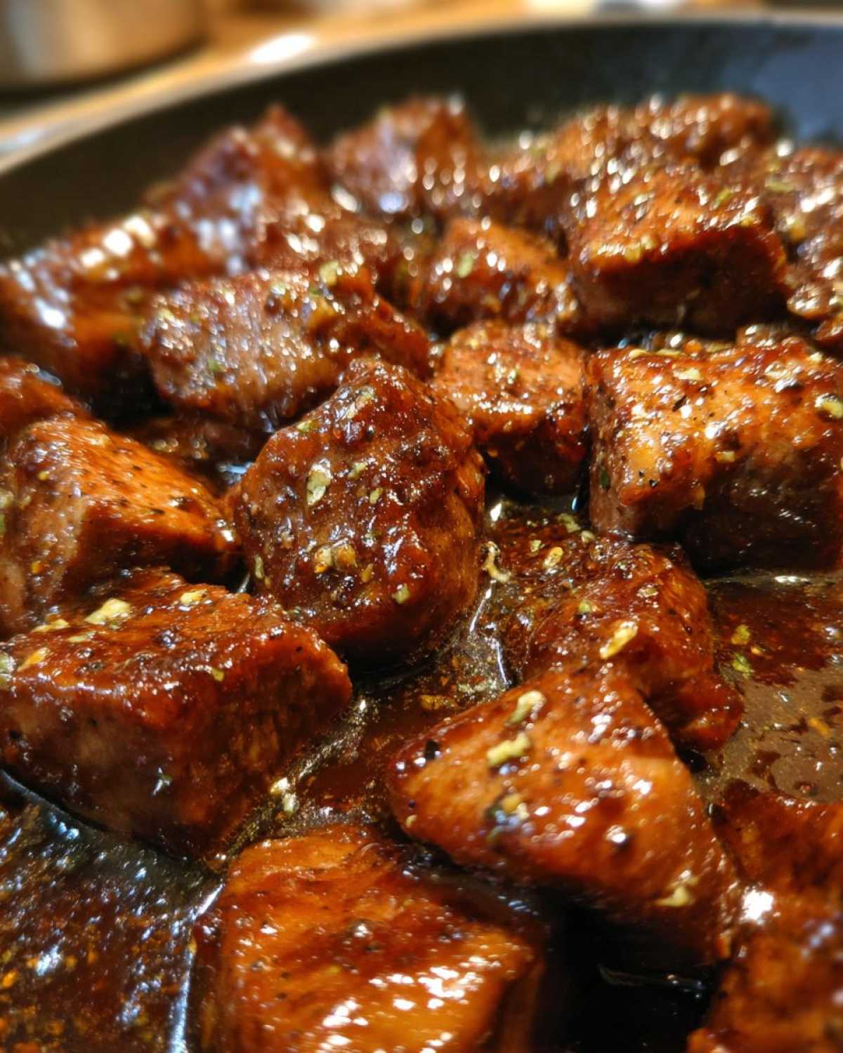 Close-up of tender crockpot steak bites coated in a thick, glossy, dark brown sauce with visible herbs.