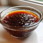 Close-up of thick, dark homemade teriyaki sauce with visible texture and sheen in a small clear glass ramekin.
