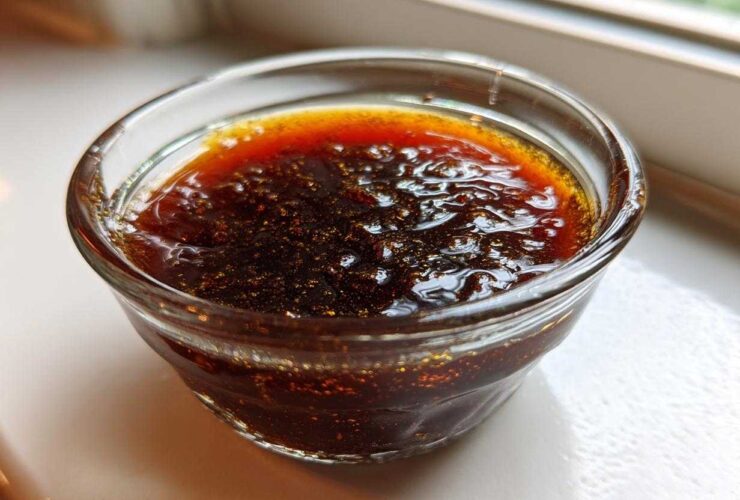 Close-up of thick, dark homemade teriyaki sauce with visible texture and sheen in a small clear glass ramekin.