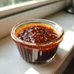 Close-up of thick, glossy homemade teriyaki sauce speckled with sesame seeds in a small glass ramekin.