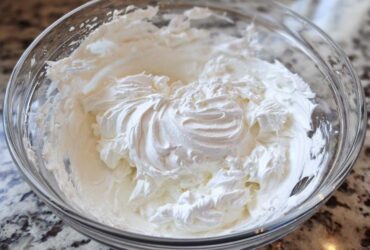 Close-up of thick, perfectly whipped white royal icing recipe mixture in a clear glass bowl.