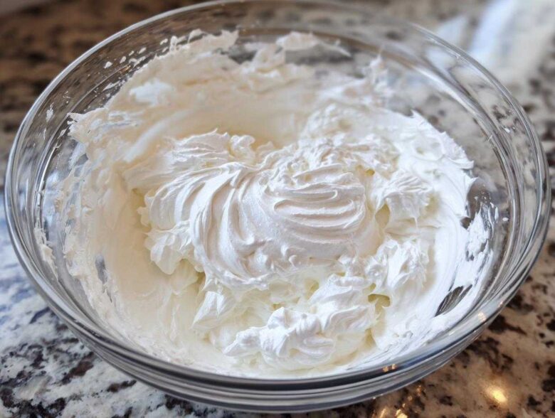 Close-up of thick, perfectly whipped white royal icing recipe mixture in a clear glass bowl.