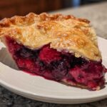 A close-up of a juicy slice of triple berry pie showing the rich berry filling and flaky golden crust.