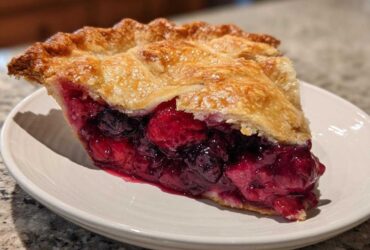 A close-up of a juicy slice of triple berry pie showing the rich berry filling and flaky golden crust.