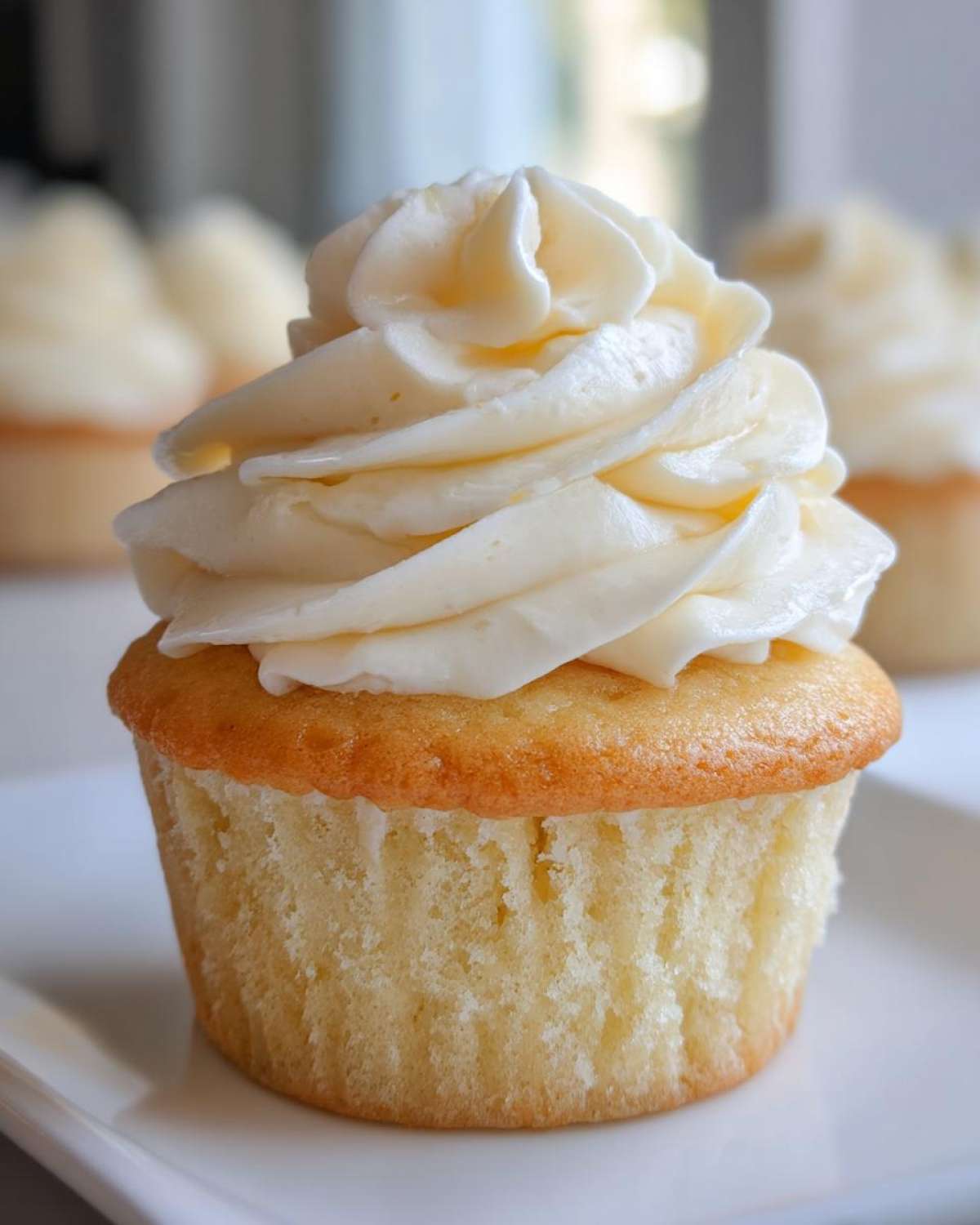 Close-up of a single, moist vanilla cupcakes topped with a tall swirl of creamy white vanilla frosting.