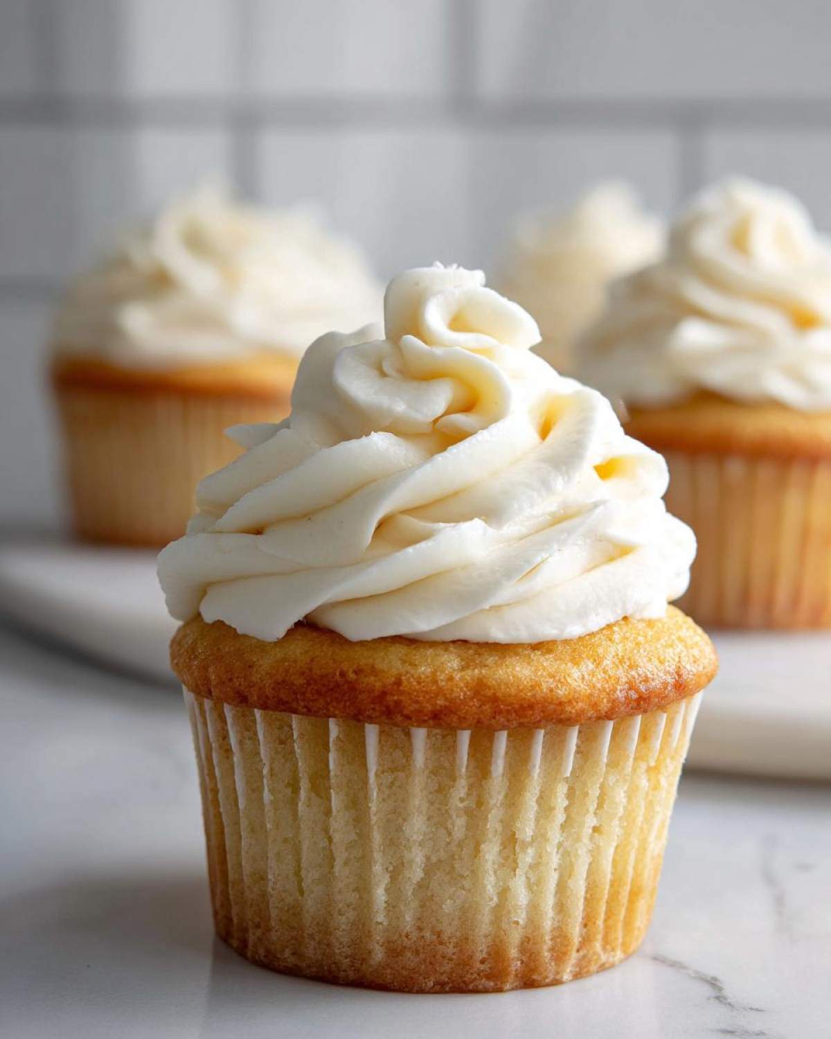 Close-up of a single vanilla cupcake topped with a tall swirl of white vanilla buttercream frosting.