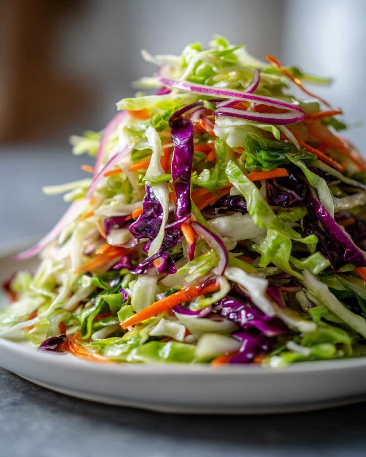Close-up of a vibrant, freshly dressed cabbage salad featuring shredded green cabbage, purple cabbage, carrots, and red onion slices.