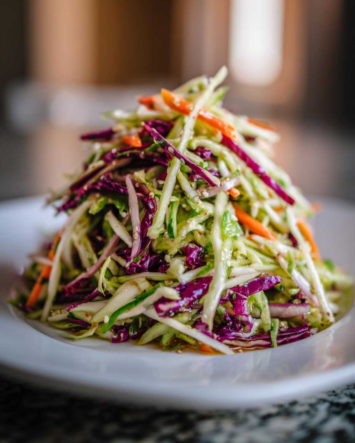 A tall mound of fresh cabbage salad featuring shredded green and purple cabbage, carrots, and a light dressing.