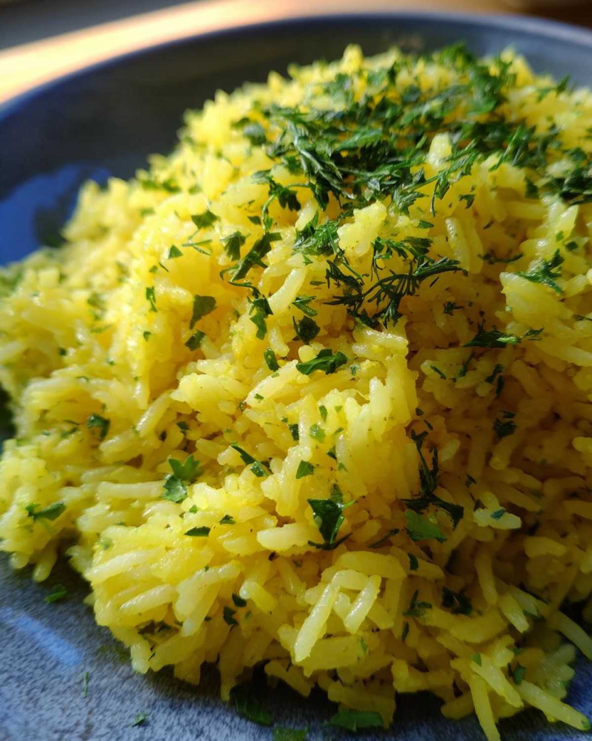 Close-up of fluffy, yellow mediterranean rice topped generously with chopped green herbs.