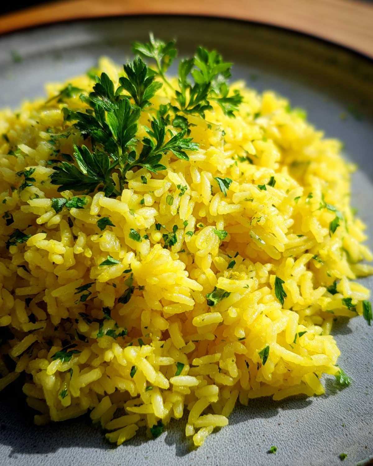 Close-up of vibrant, yellow mediterranean rice garnished with fresh chopped parsley on a grey plate.