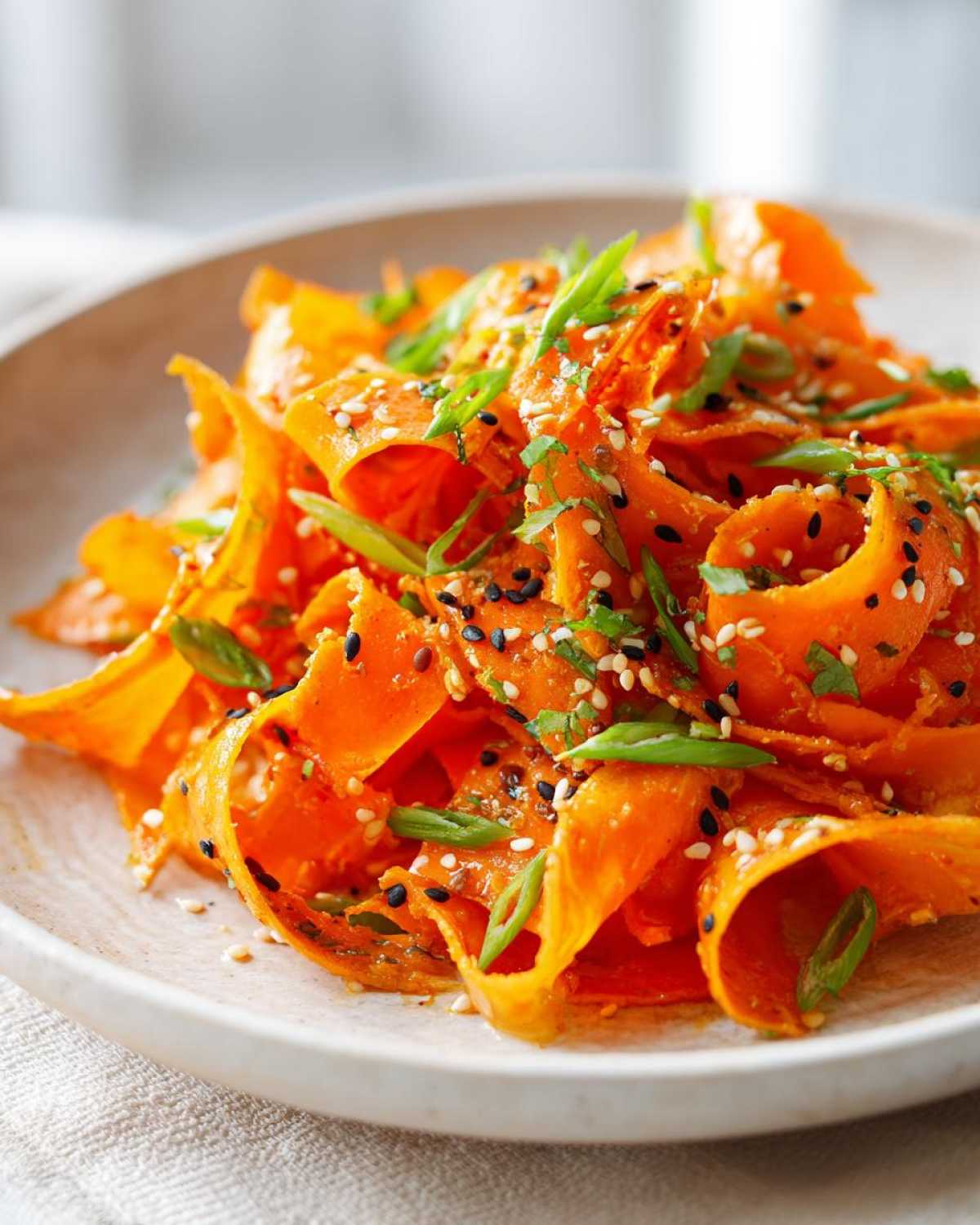 Close-up of vibrant raw carrot salad ribbons tossed with sesame seeds and green onions.
