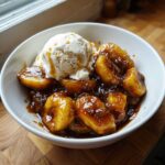Close-up of warm bananas foster caramelized in rich sauce topped with a scoop of vanilla ice cream.