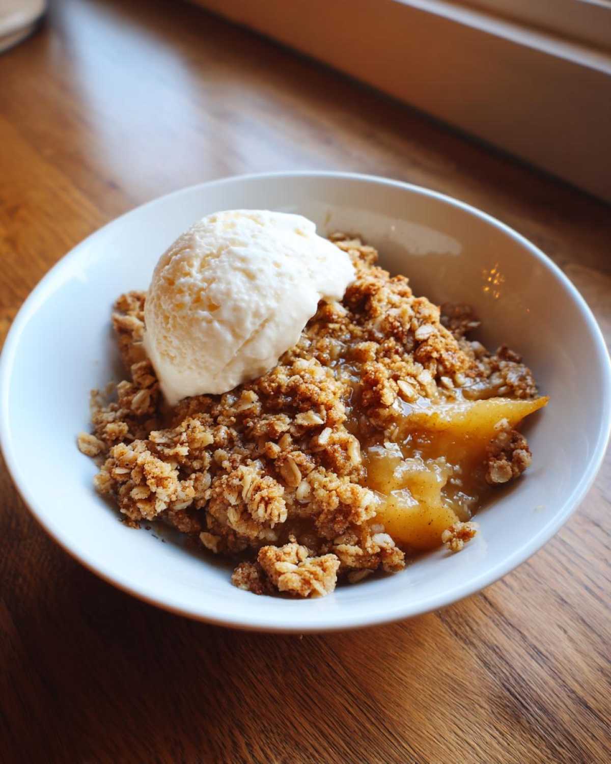 A warm serving of pear crisp with a crunchy topping and a scoop of vanilla ice cream on top.