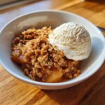 A warm serving of homemade pear crisp topped with a scoop of vanilla ice cream in a white bowl.