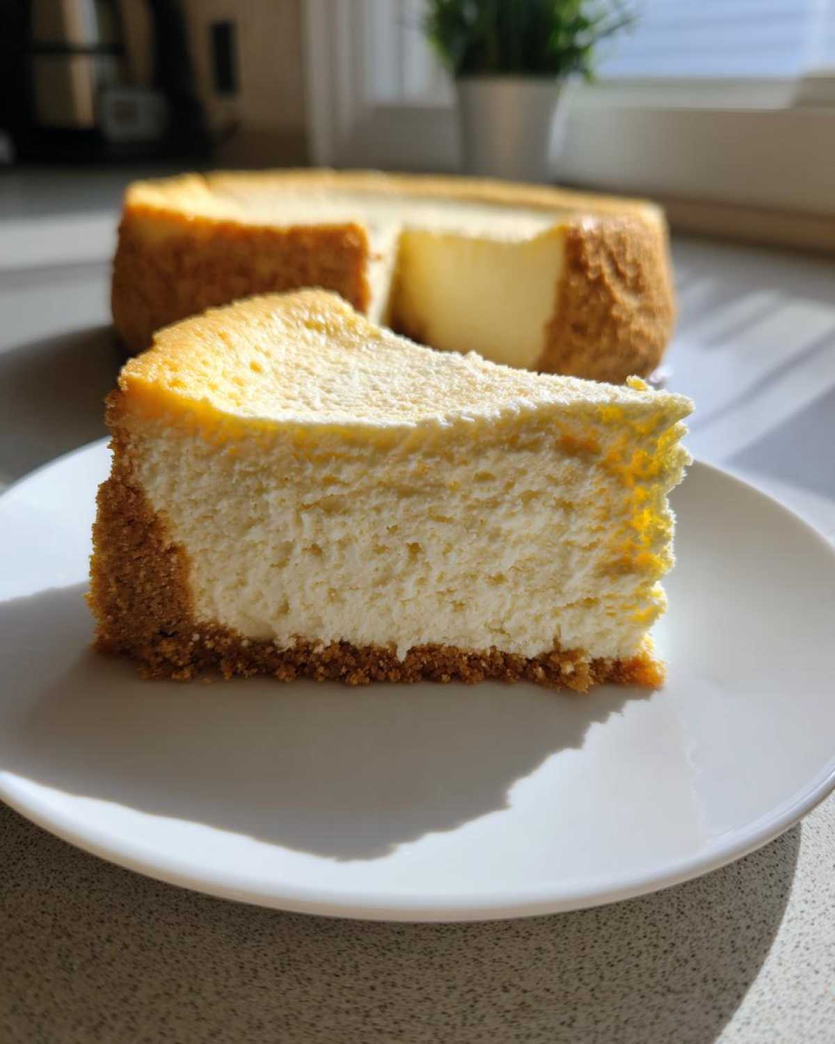 A perfect slice of creamy white chocolate cheesecake with a graham cracker crust on a white plate.