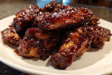 A pile of juicy, sticky Air Fryer BBQ Chicken Wings coated in dark, rich sauce on a white plate.