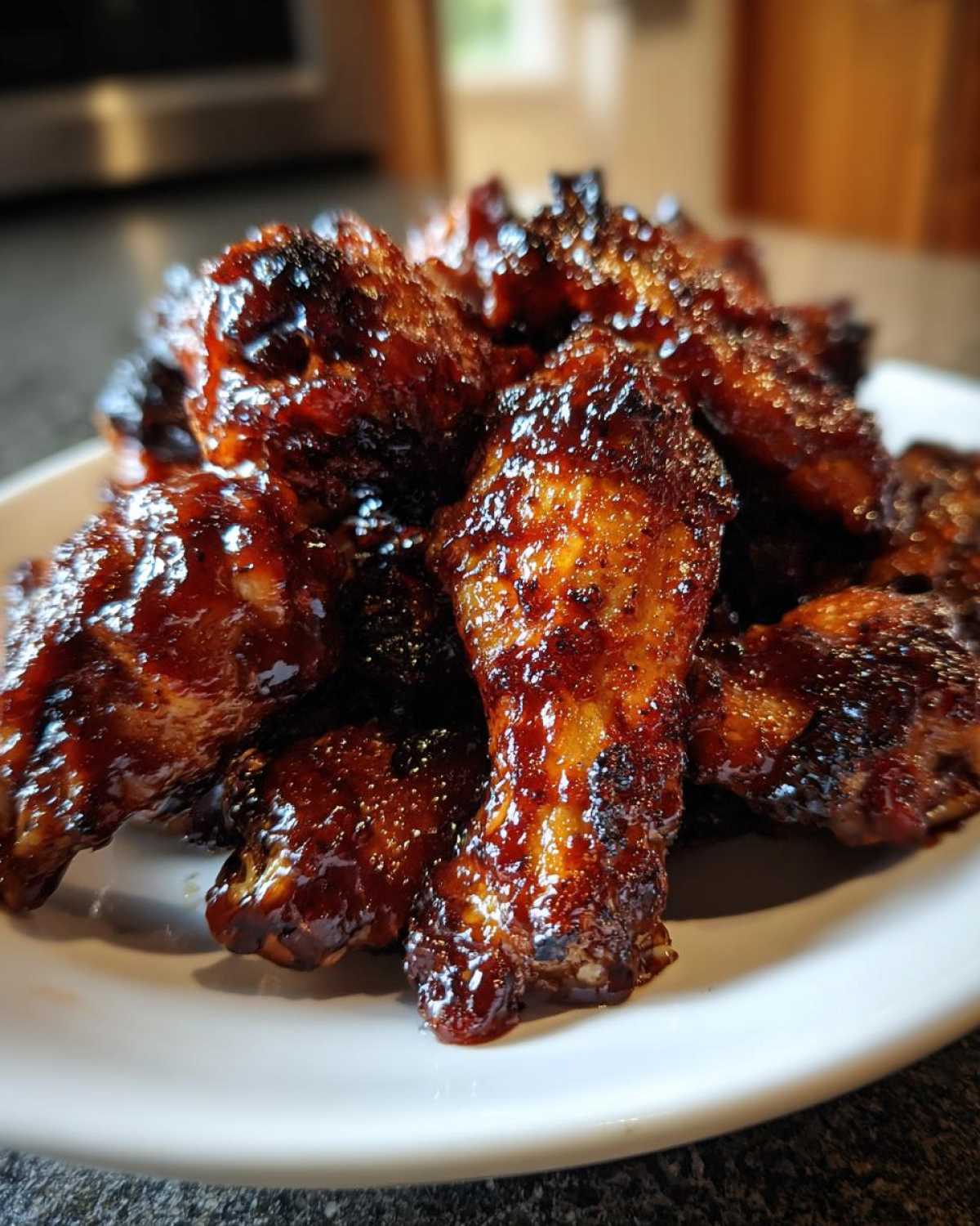 Close-up of sticky, caramelized Air Fryer BBQ Chicken Wings piled high on a white plate.
