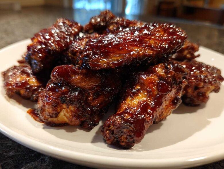 A pile of juicy, sticky Air Fryer BBQ Chicken Wings coated in dark, rich sauce on a white plate.
