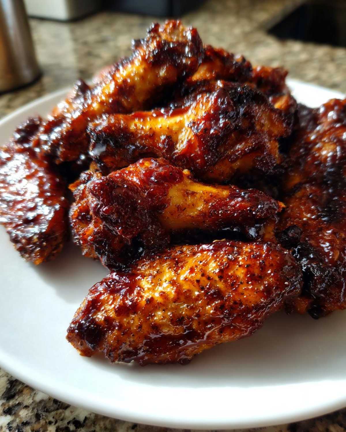 A close-up of crispy, saucy Air Fryer BBQ Chicken Wings piled high on a white plate.