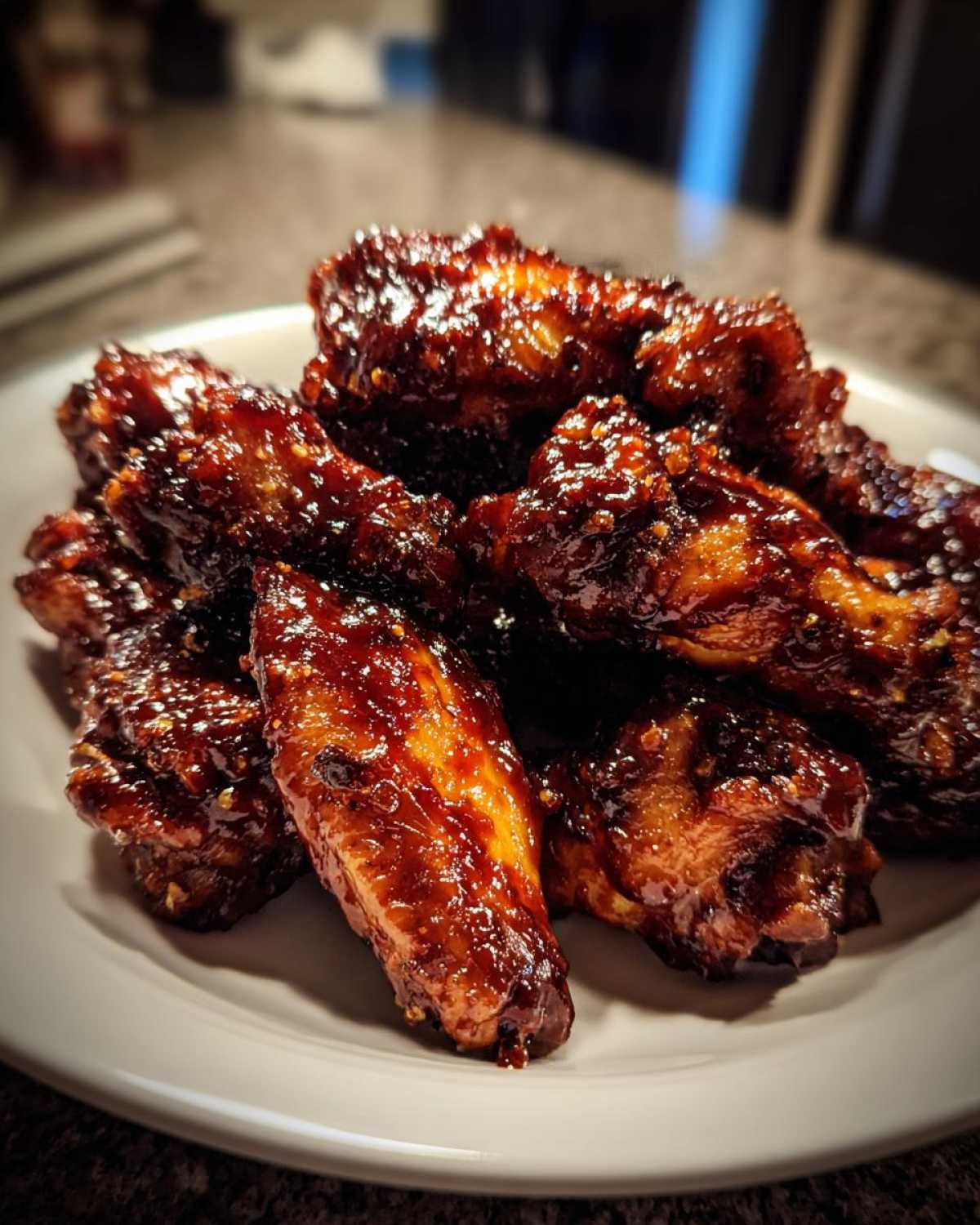 A close-up of a pile of sticky, dark, glazed Air Fryer BBQ Chicken Wings on a white plate.