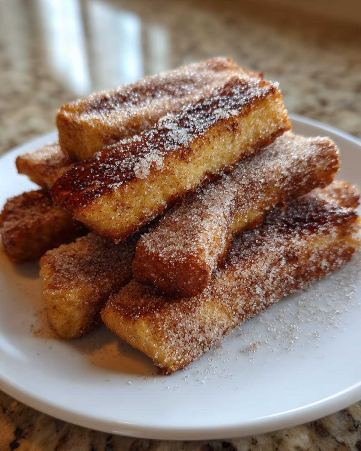A stack of golden brown Air Fryer French Toast Sticks generously coated in sparkling cinnamon sugar on a white plate.