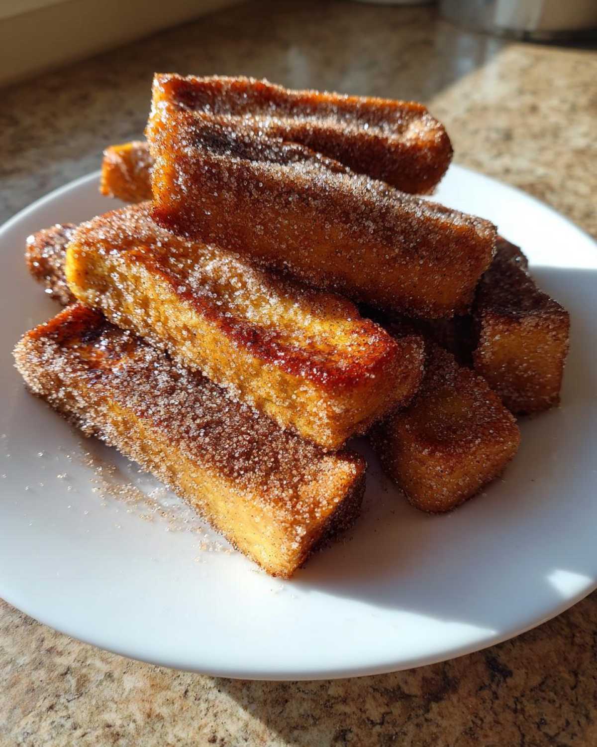 A pile of golden brown Air Fryer French Toast Sticks heavily coated in cinnamon sugar, served on a white plate.