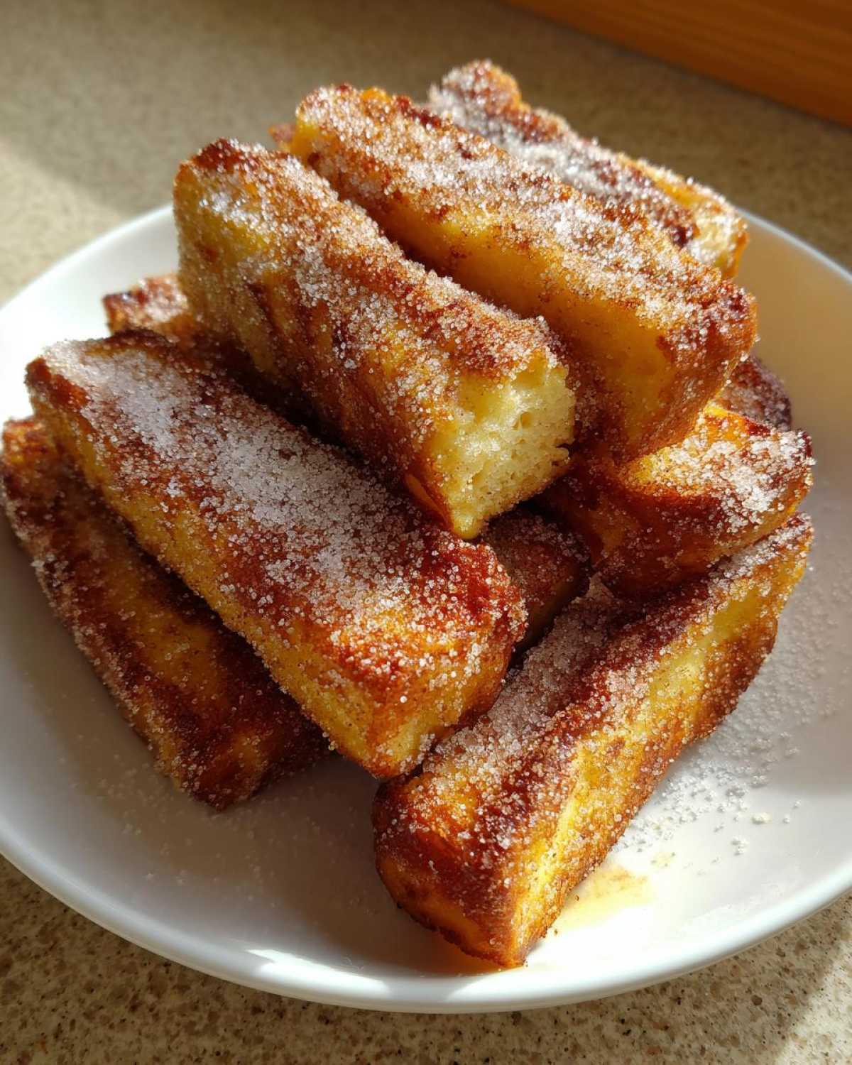 A stack of golden brown Air Fryer French Toast Sticks heavily coated in sparkling cinnamon sugar on a white plate.