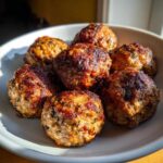 A close-up shot of seven golden-brown, perfectly cooked Air Fryer Italian Meatballs piled in a light-colored bowl.