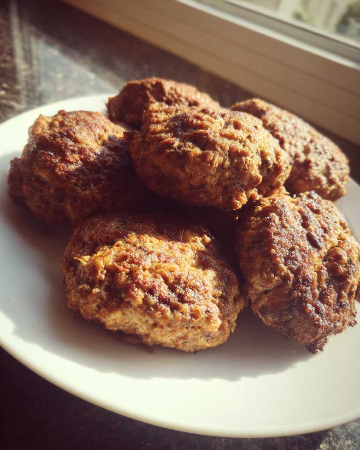 A pile of perfectly browned Air Fryer Italian Meatballs resting on a white plate near a sunlit window.