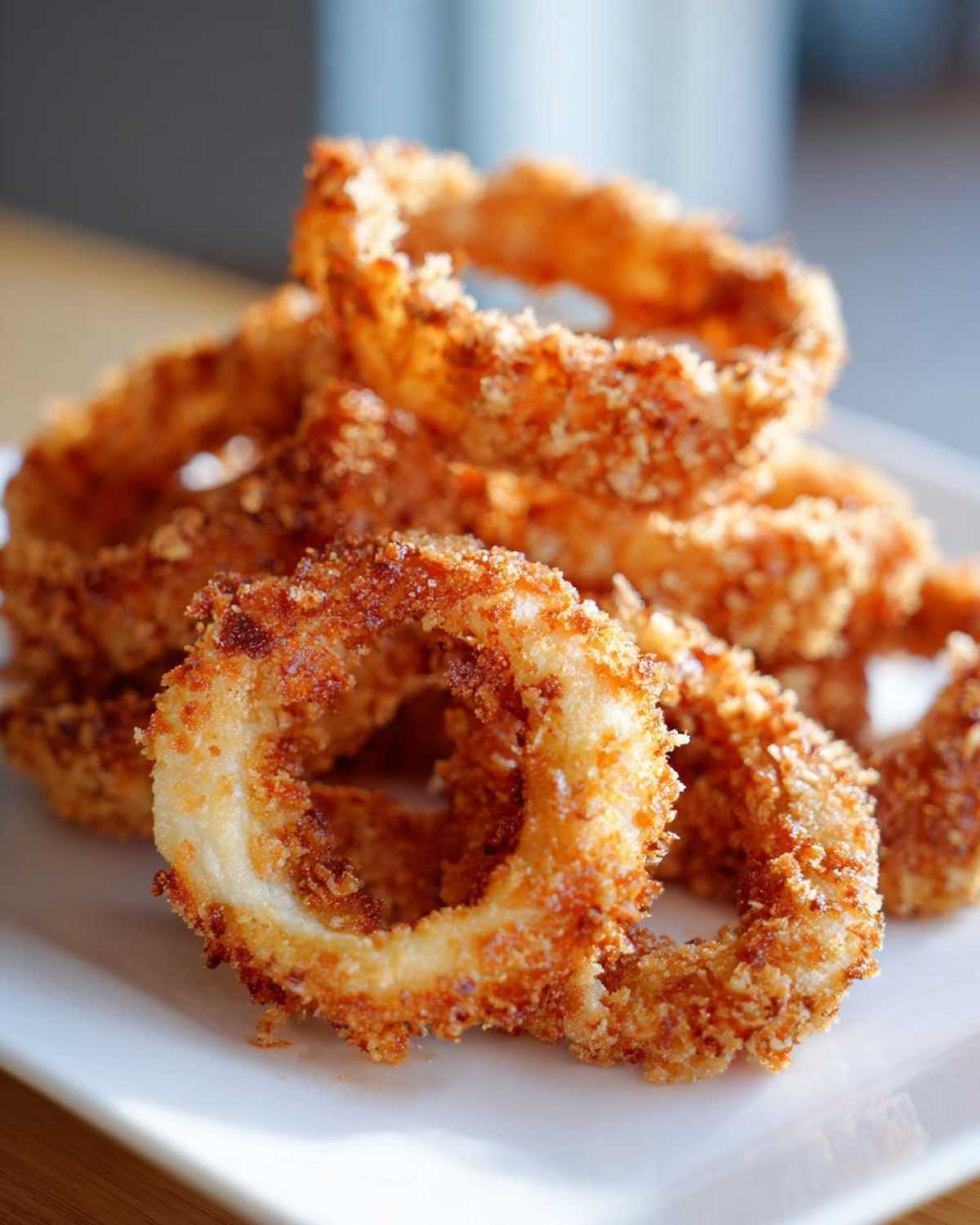 A close-up of a stack of golden brown, crispy Air Fryer Onion Rings on a white plate.