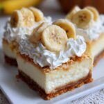 A close-up of a square slice of Banana Pudding Cheesecake Bars topped with whipped cream and fresh banana slices.