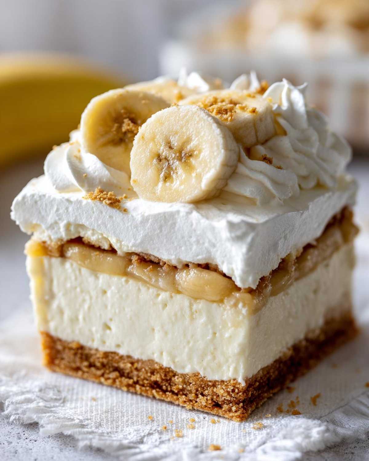 Close-up of a layered Banana Pudding Cheesecake Bars square topped with whipped cream, banana slices, and crumbs.