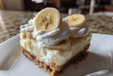 A single serving slice of Banana Pudding Cheesecake Bars topped with whipped cream and fresh banana slices.