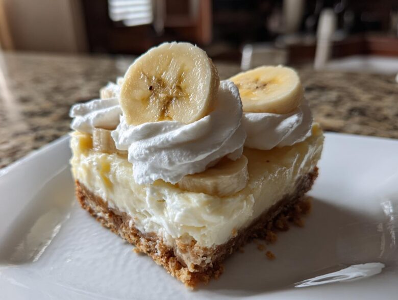 A single serving slice of Banana Pudding Cheesecake Bars topped with whipped cream and fresh banana slices.
