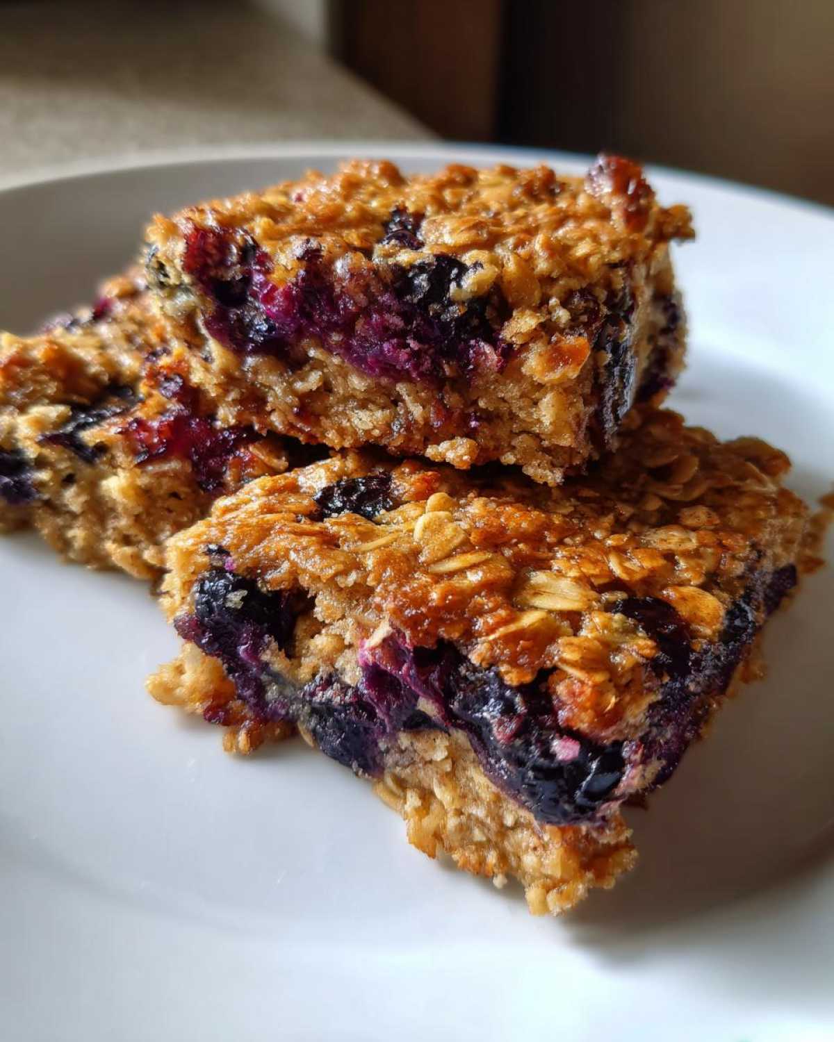 A close-up stack of two rich, golden Blueberry Baked Oatmeal Squares showing visible oats and juicy baked blueberries.