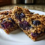 Close-up of two moist Blueberry Baked Oatmeal Squares showing oats and bursting blueberries.