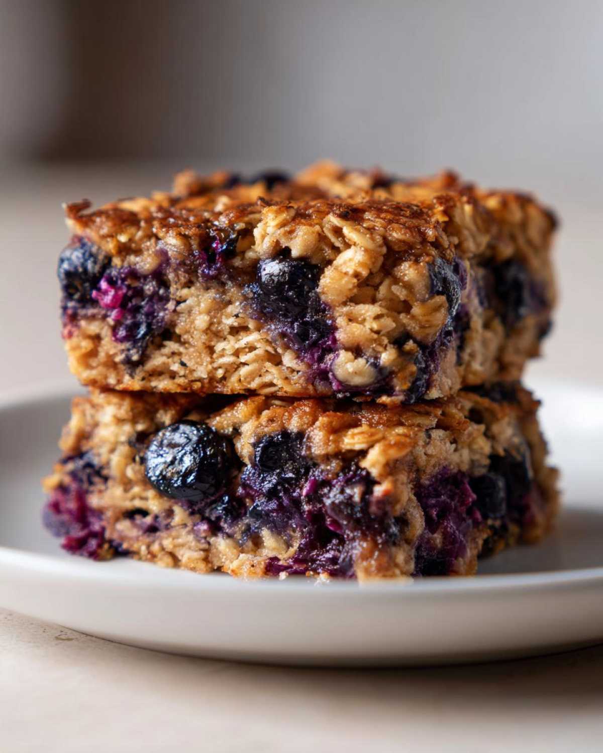 Close-up of two stacked Blueberry Baked Oatmeal Squares showing oats and bursts of purple blueberries.