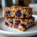 Two stacked, golden-brown Blueberry Baked Oatmeal Squares featuring visible oats and juicy baked blueberries.