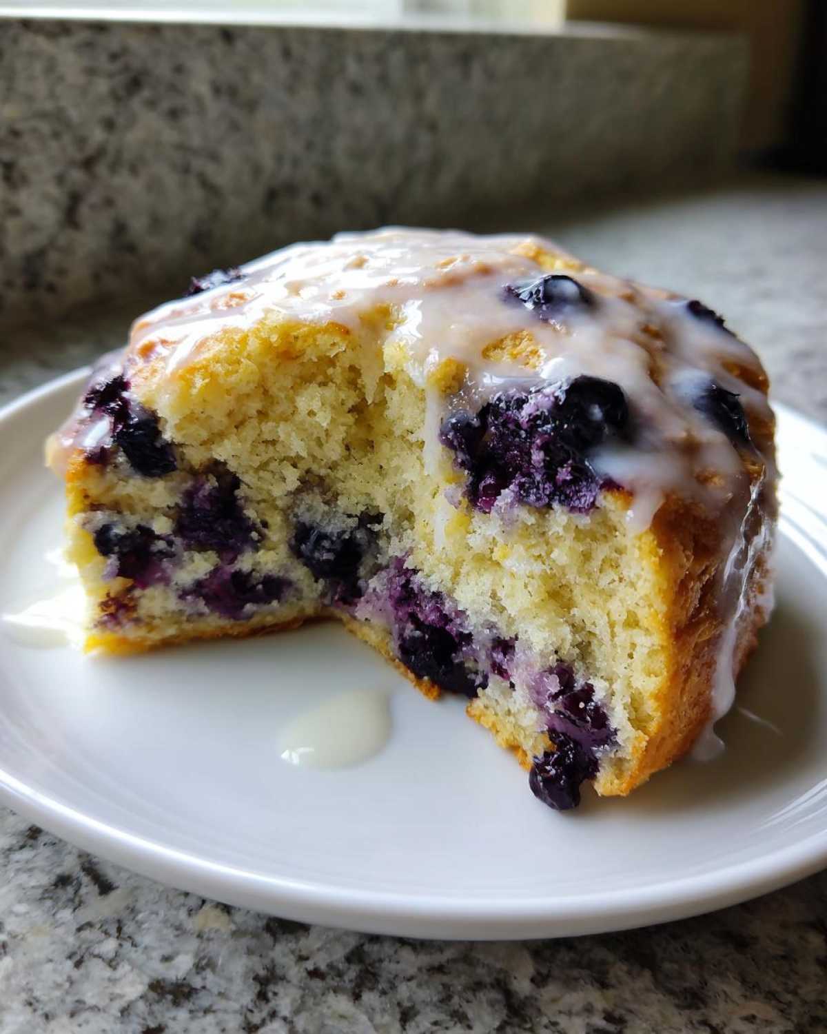 A cross-section of a Blueberry Lemon Scones piece showing the moist interior packed with blueberries and topped with lemon glaze.
